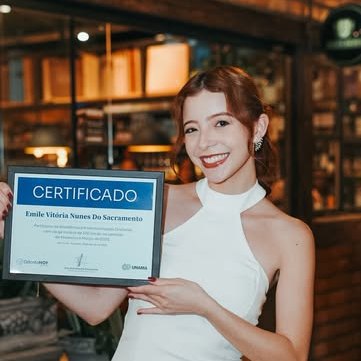 Dra. Emile Vitória segurando o certificado de conclusão da residência em Harmonização Orofacial